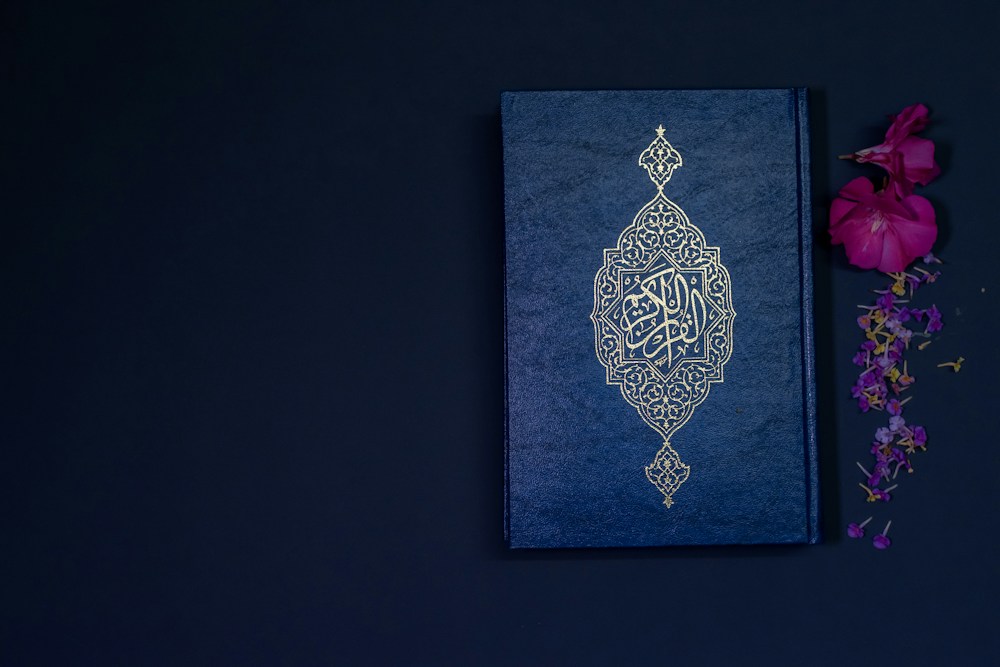 A Quran with a gold patterned cover beside flowers
